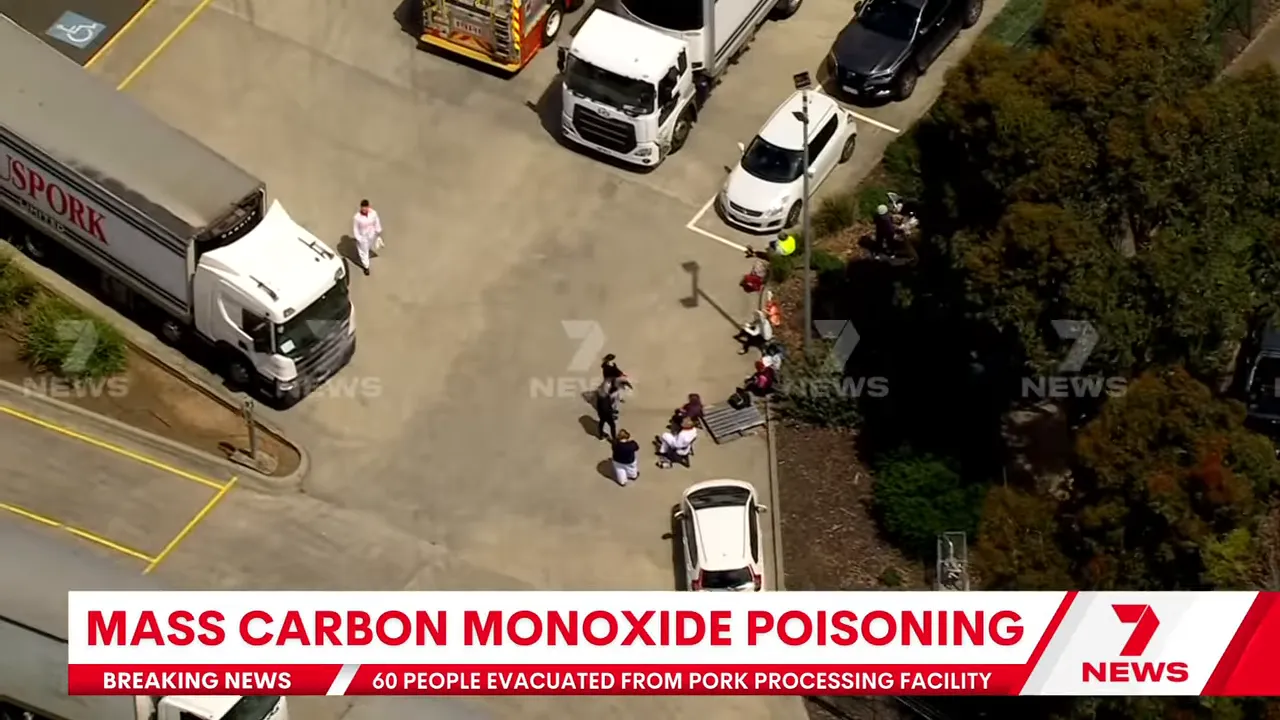 Aerial close-up of evacuated workers seated near an AusPork truck with responders nearby