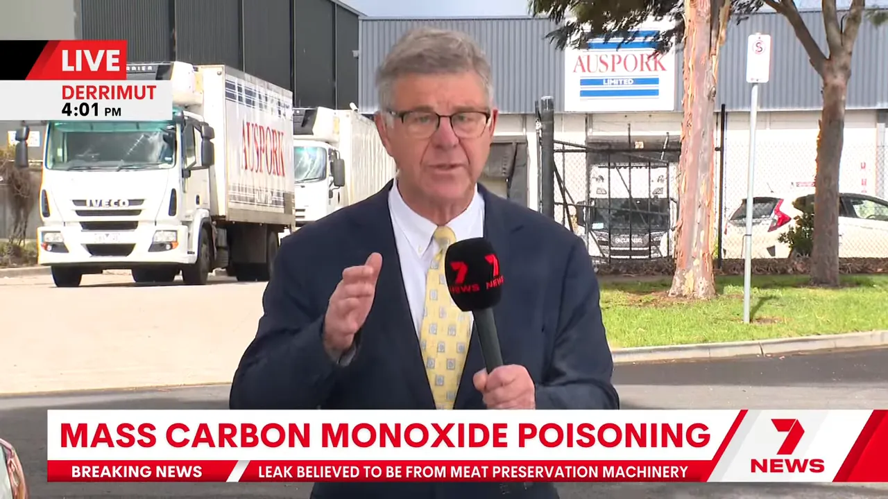 Wide shot of TV reporter outside AusPork facility showing trucks and building signage, breaking news about carbon monoxide