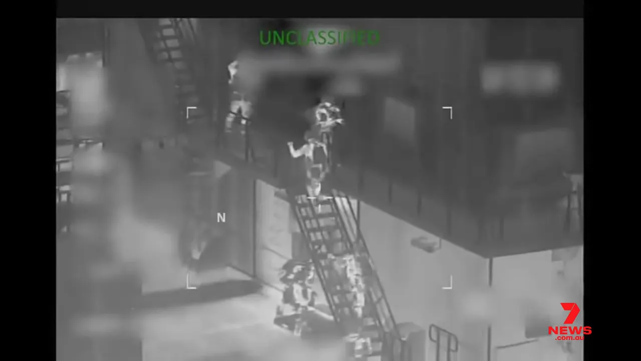 Clear thermal surveillance image of several personnel using a gangway/ladder to board a vessel; 'UNCLASSIFIED' label visible at top and news watermark at bottom right.