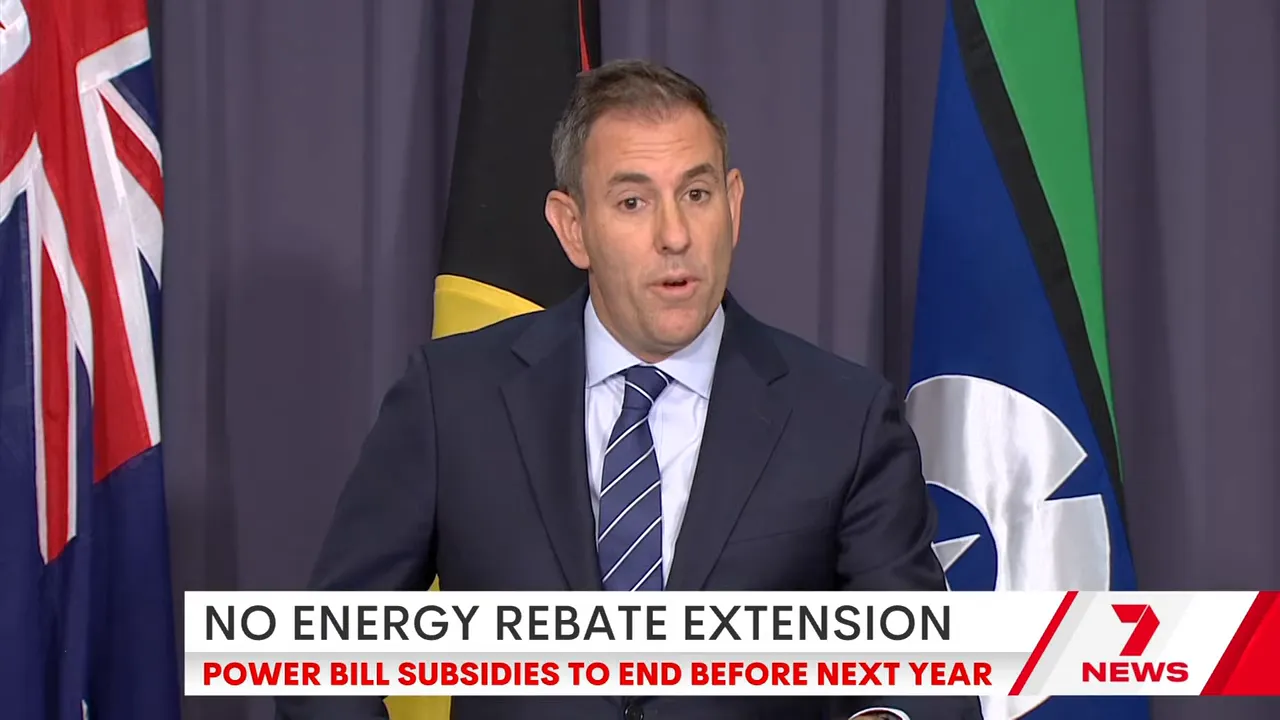 Government official at a podium delivering a statement with flags behind and a news headline about no energy rebate extension