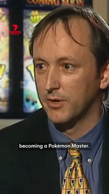 Television interview frame of a man discussing becoming a Pokémon Master with Pokémon posters behind him