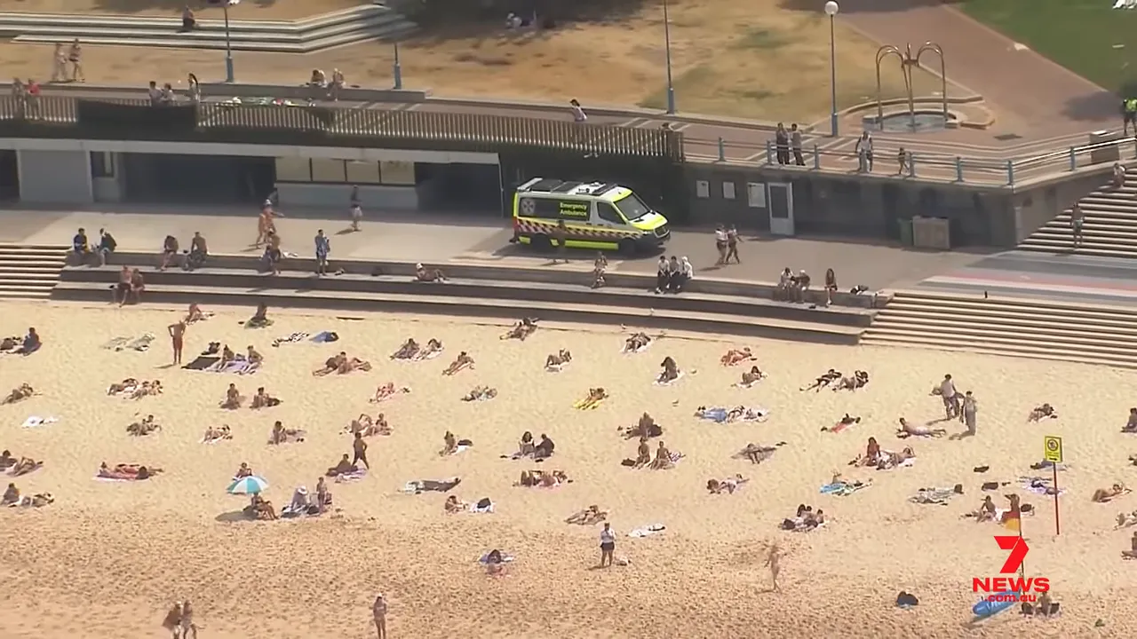 aerial view of sunbathers on a sandy beach and an emergency ambulance on the promenade
