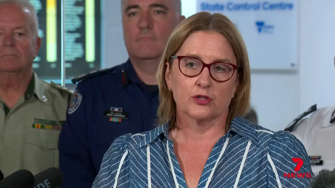 Senior emergency services official speaking at a control-centre press briefing with microphones and team members visible