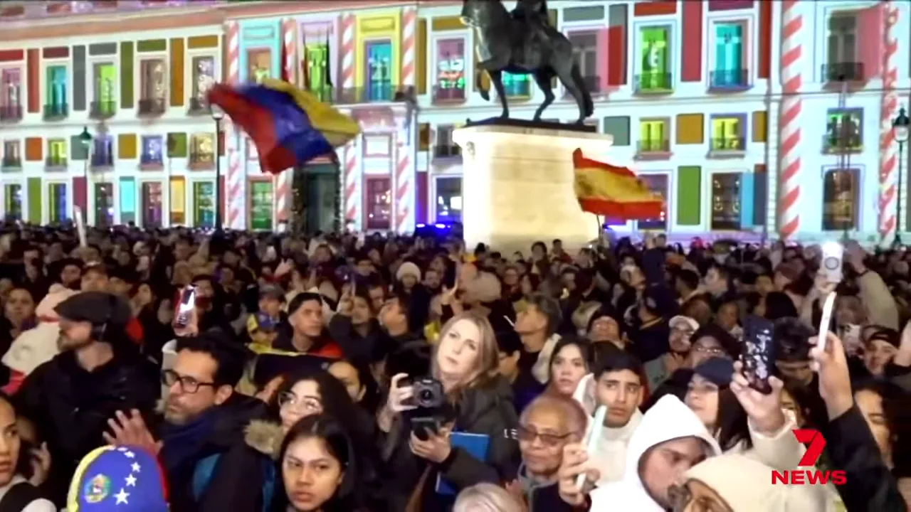 Large crowd gathered in a city square at night waving Venezuelan flags