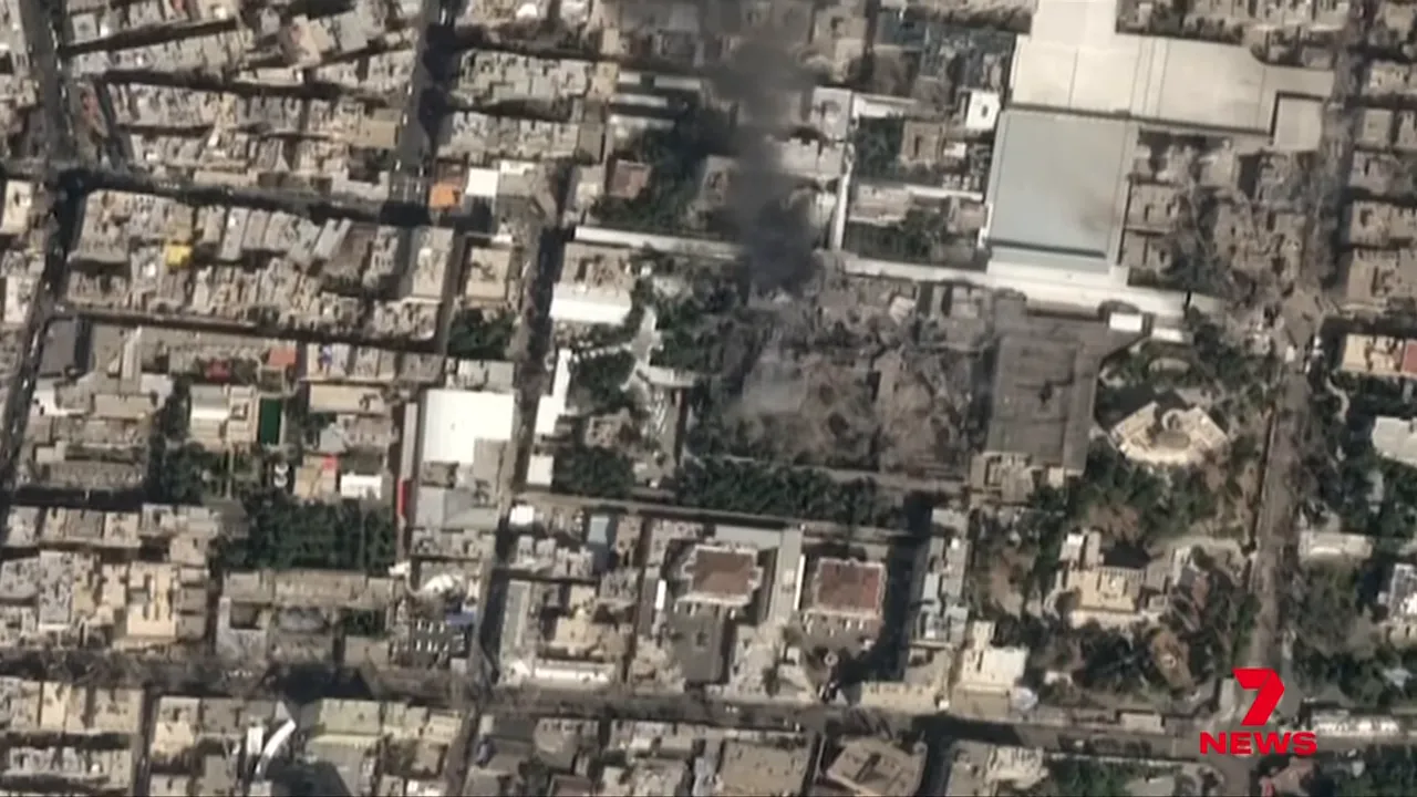 High-angle aerial image of a dense urban area with a clear plume of dark smoke rising from a specific compound.