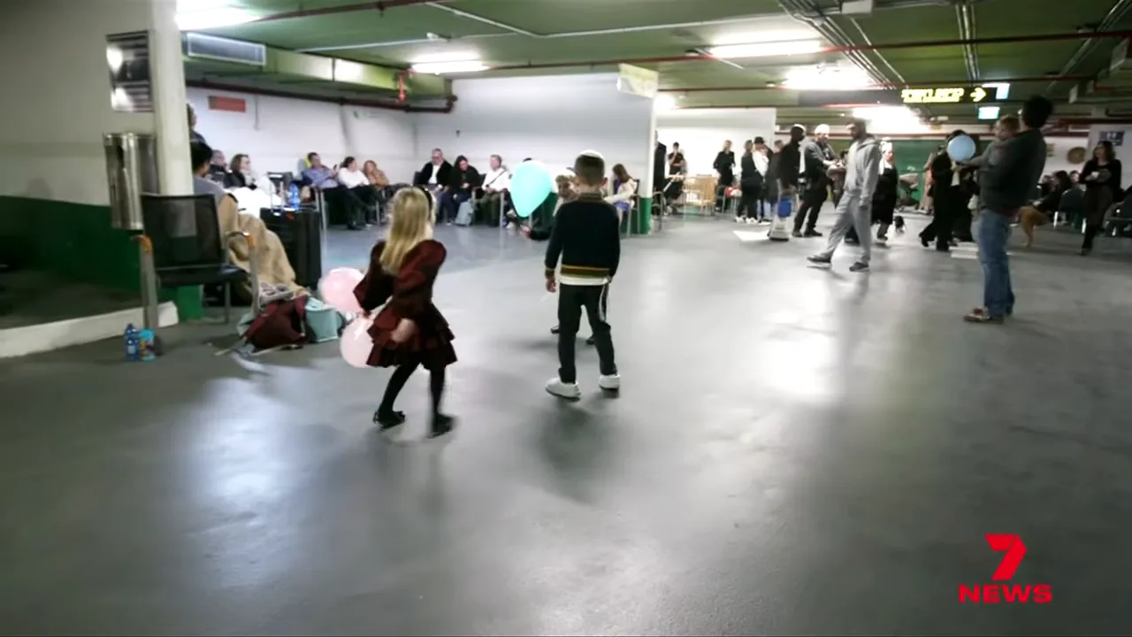 Wide view of families and children gathered in an underground carpark converted to a shelter