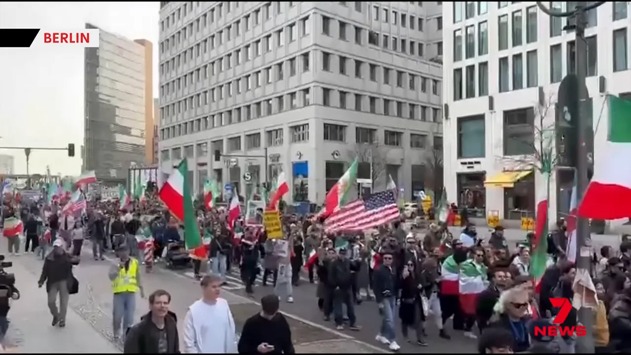 Wide shot of a large street march in Berlin with numerous flags including US and Iranian flags