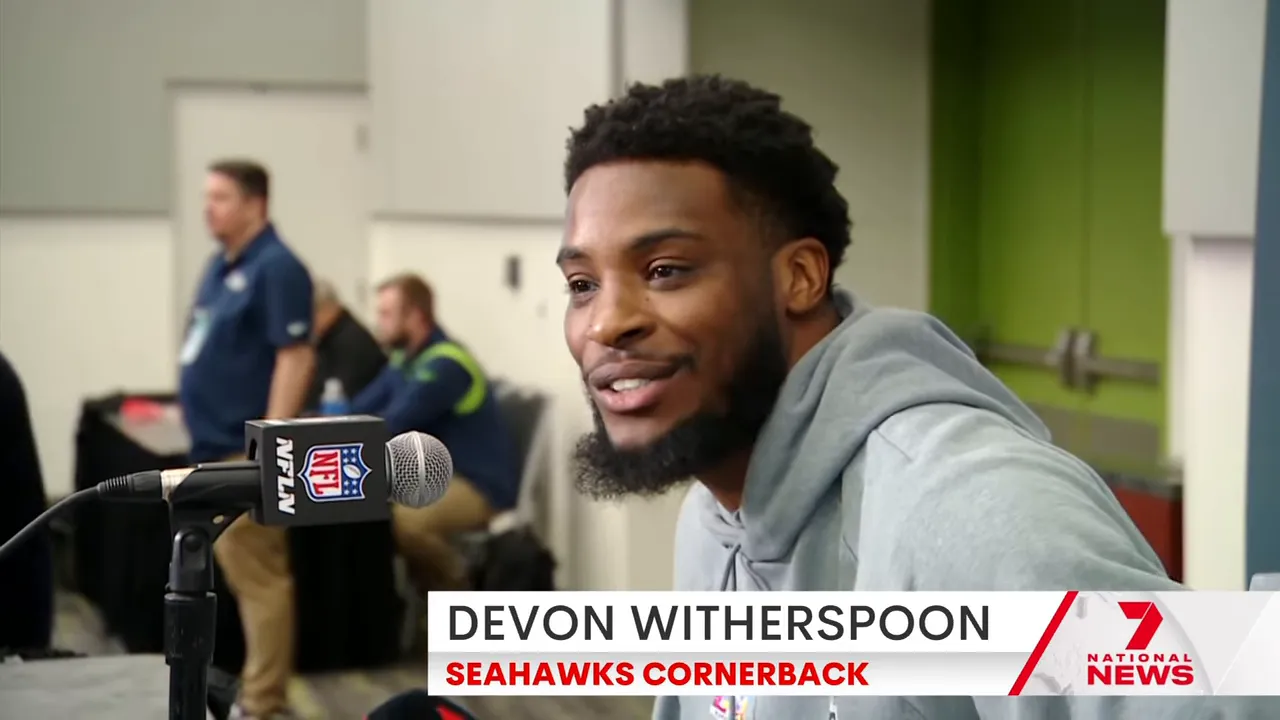 Close-up of a Seahawks player smiling while speaking into an NFL microphone at a press conference.