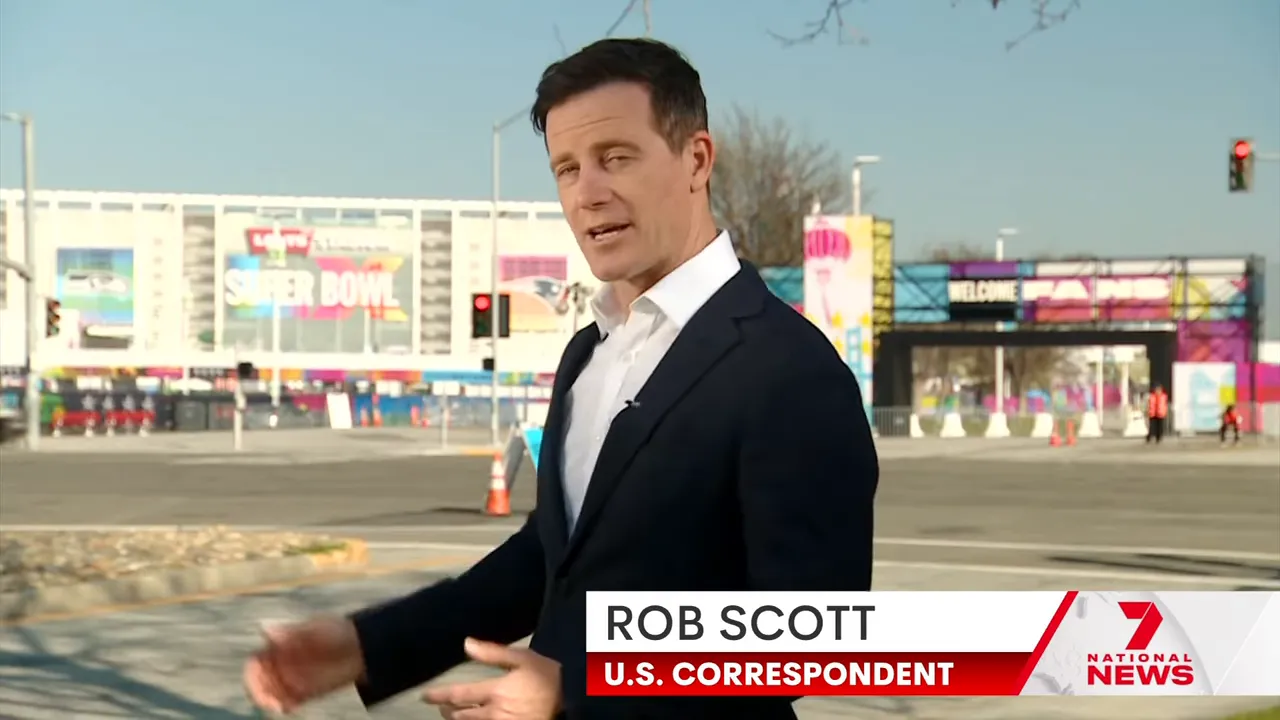 Reporter standing outside stadium entrance with large 'Super Bowl' signage and colourful fan-zone banners
