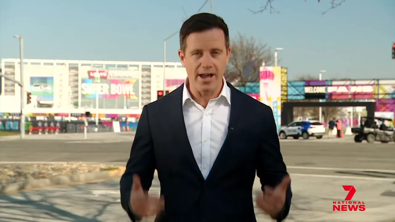 Field reporter standing outside Levi's Stadium with Super Bowl signage and the fan zone visible behind him