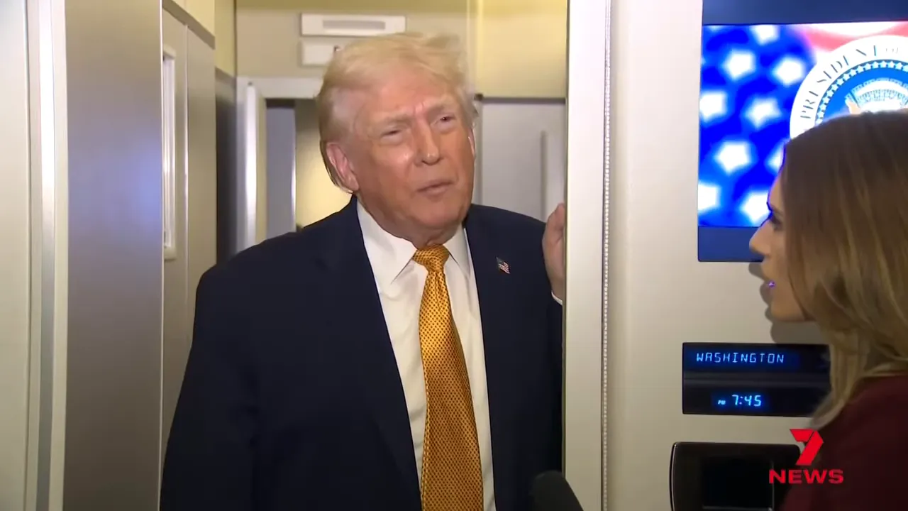 Senior US leader speaking to a reporter in an aircraft aisle with a TV showing a seal and a 'WASHINGTON' time display