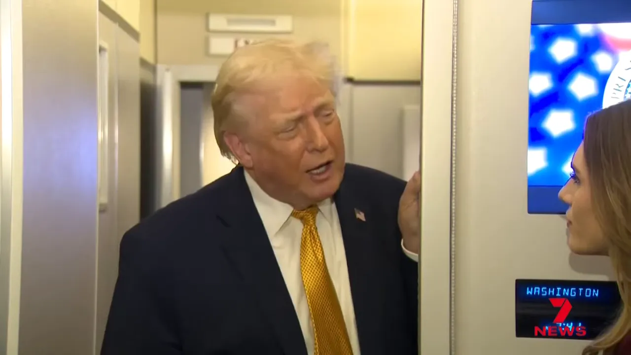 Man speaking to a reporter beside an interior aircraft panel during a press exchange