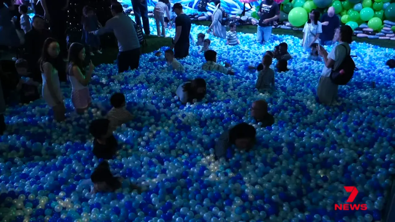 Wide view of a crowded immersive ball-pit area filled with blue and white plastic/balloon balls and families playing inside.