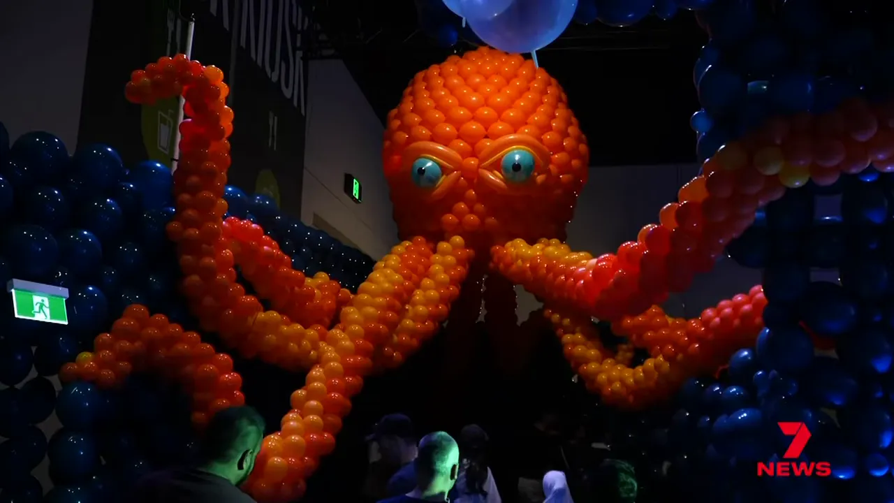 Large orange octopus sculpture made from thousands of balloons filling a dark exhibition hall, showing scale and detail.