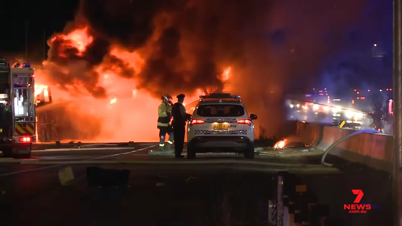 Police vehicle and firefighters in front of a large truck fire and heavy smoke on the motorway