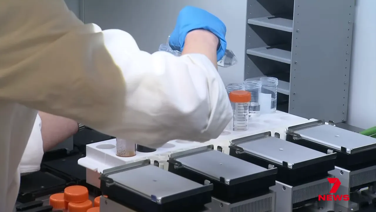 Technician handling sample vials next to automated laboratory instruments and plates.