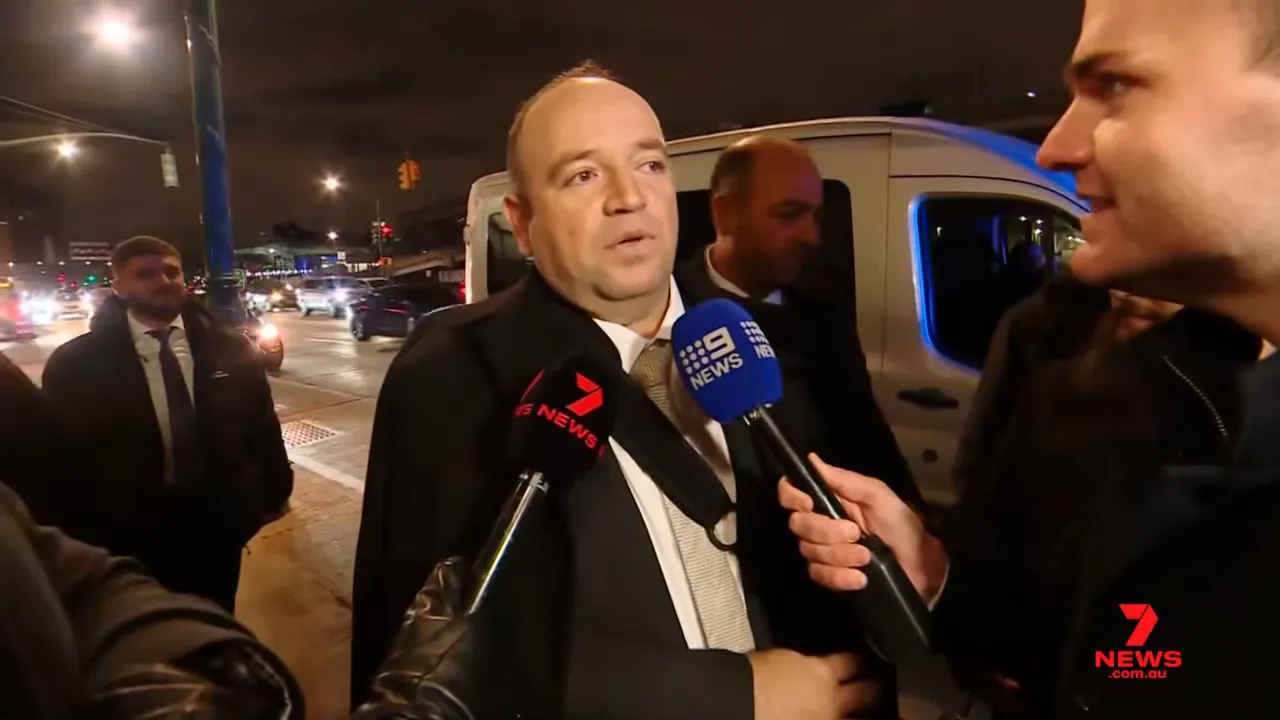 Ahmed Al Ahmed answering questions from reporters by a van at night, 9 News microphone visible.