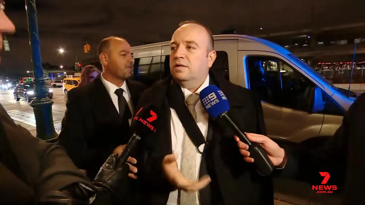 Night-time curbside interview: man speaking to reporters with 7 News and 9 News microphones and a support vehicle behind