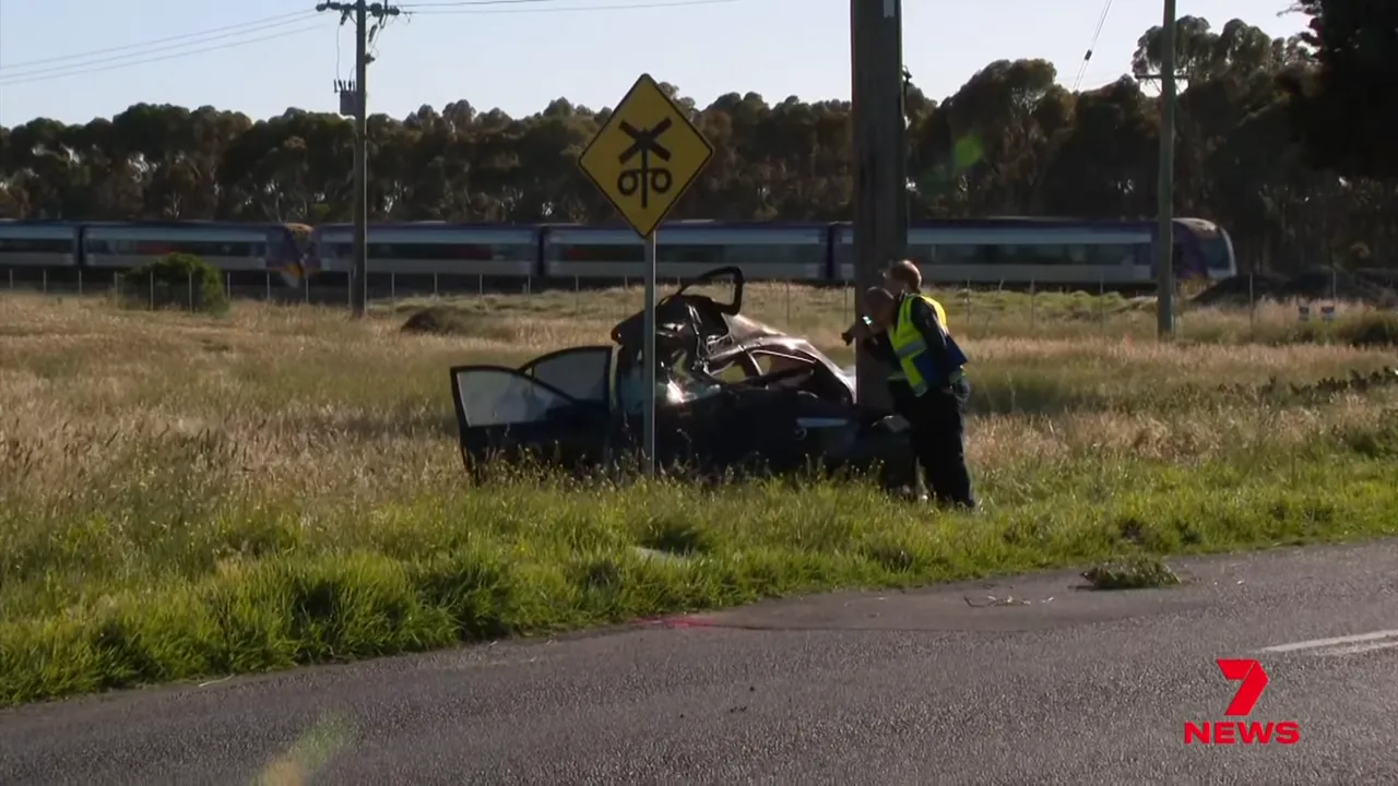 Investigators examining a heavily damaged car beside a power pole at the crash site on a grassy verge.