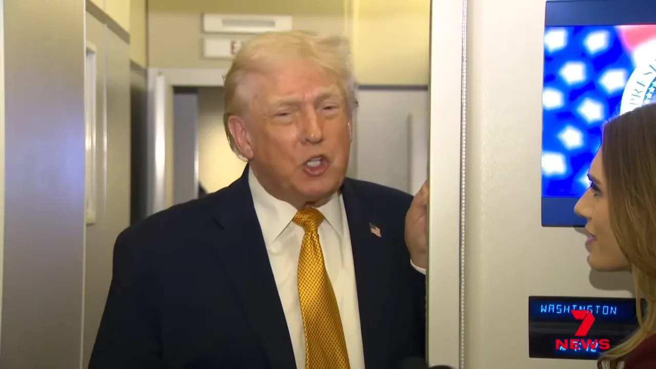 A man in a suit speaking to a reporter in an airplane doorway, framed mid-shot.