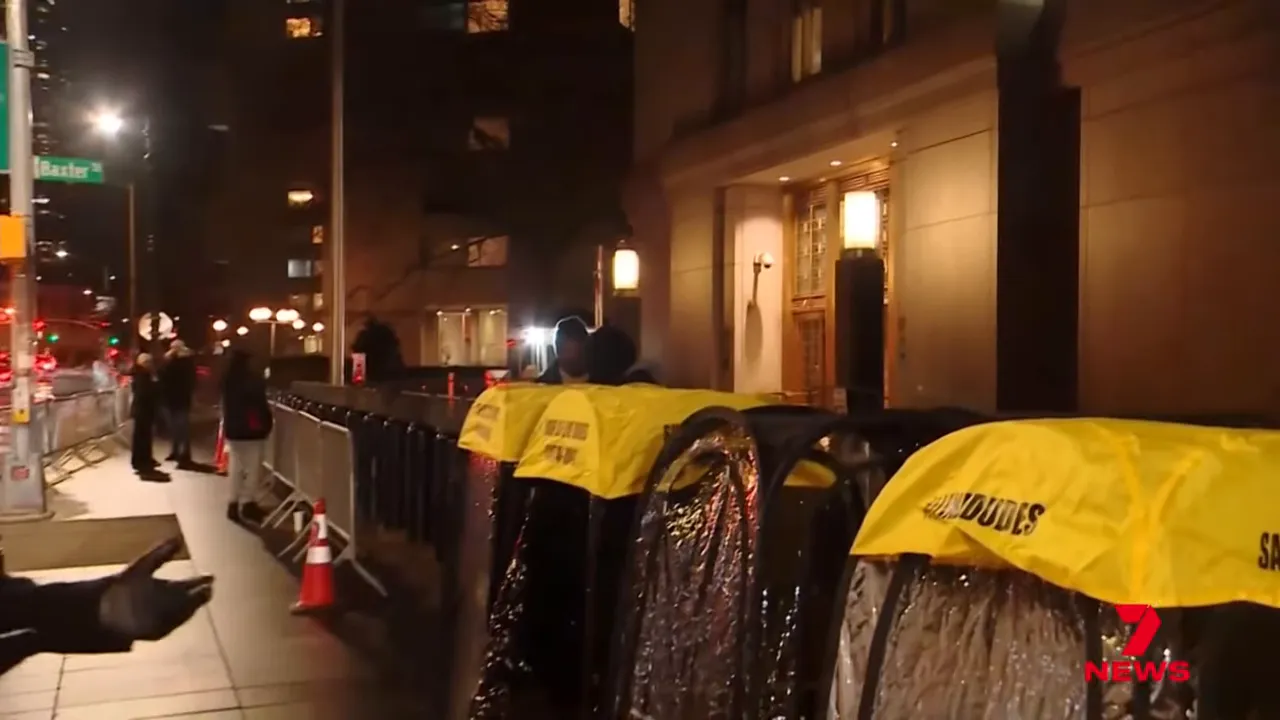 Row of small covered tents with yellow tops and barricades along a city sidewalk outside a courthouse at night.