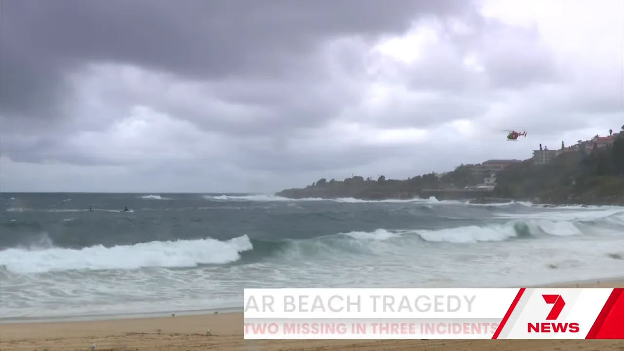 Wide view of rough surf and coastline with a rescue helicopter flying above the water near breaking waves.