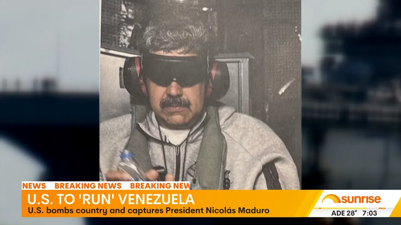 Centered broadcast image of a blindfolded man wearing ear protection and a jacket