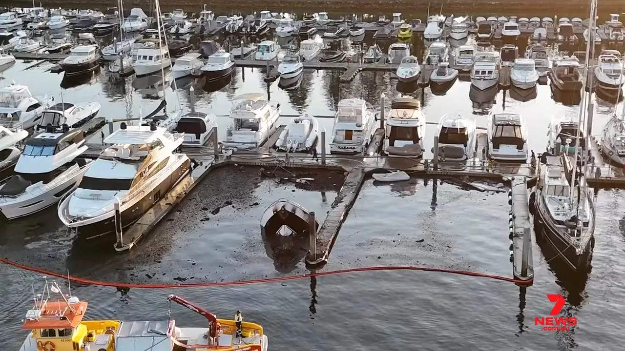 High-resolution aerial image of Spit Bridge Marina showing sunken yachts, a red containment boom and adjacent vessels.