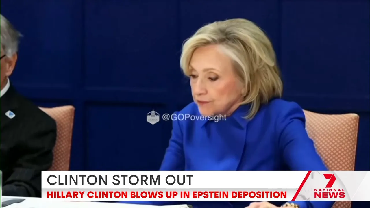 Side-view screenshot of a woman in a blue jacket at a hearing table, appearing to react to proceedings, with a news banner along the bottom.