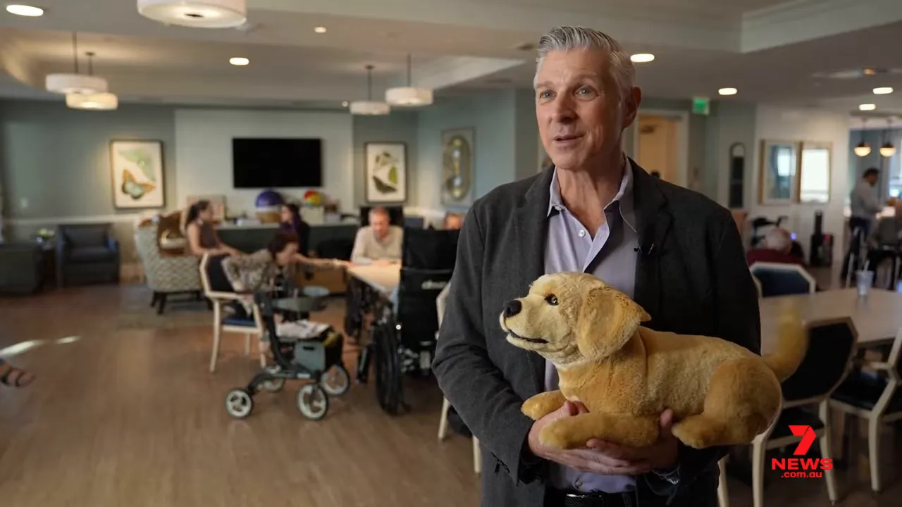 CEO demonstrating a lifelike robotic puppy in an aged-care common room
