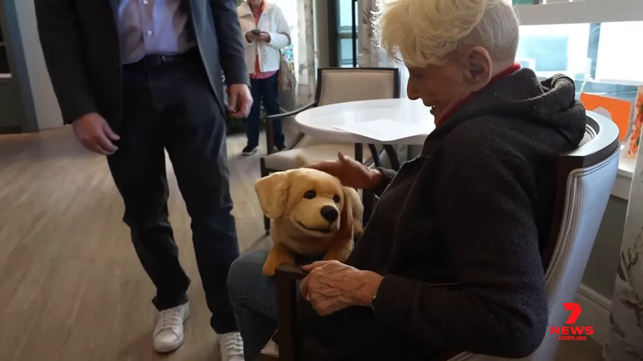 Older woman interacting with a lifelike robotic puppy on her lap in a care facility, clearly engaging with the device