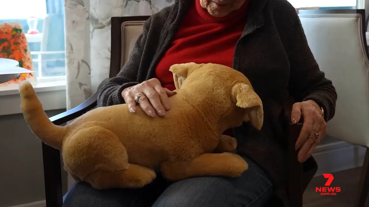 Senior petting a lifelike robotic puppy on their lap in a care facility