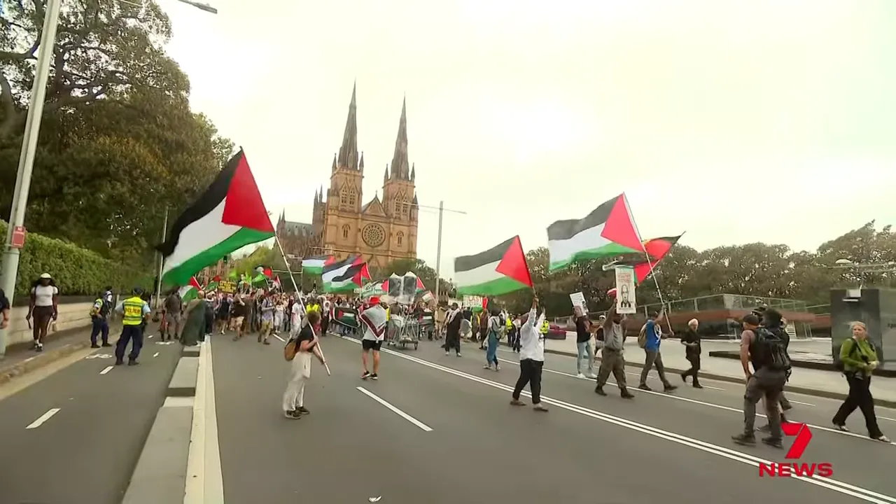 Wide shot of protesters with Palestinian flags marching on a city street near a cathedral