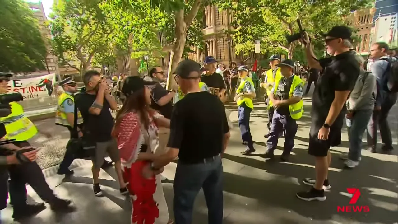 Police officers in high-visibility vests and demonstrators on a city street with media present