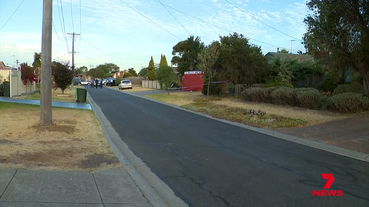 Wide shot of a residential street with police vehicles and a cordoned area in the distance on Jackman Court