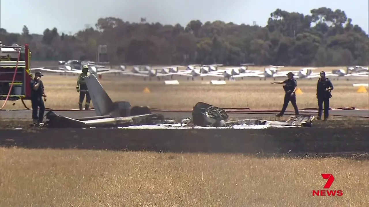 Destroyed Cessna wreckage on grass with firefighters and rows of parked training aircraft in the background at Parafield Airport