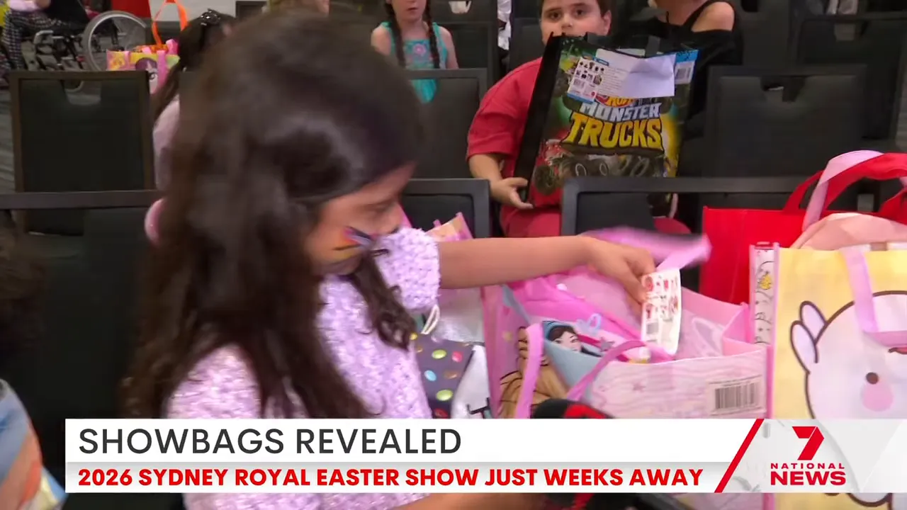Child reaching into a pink showbag filled with toys at a preview event, with other showbags and children visible nearby.