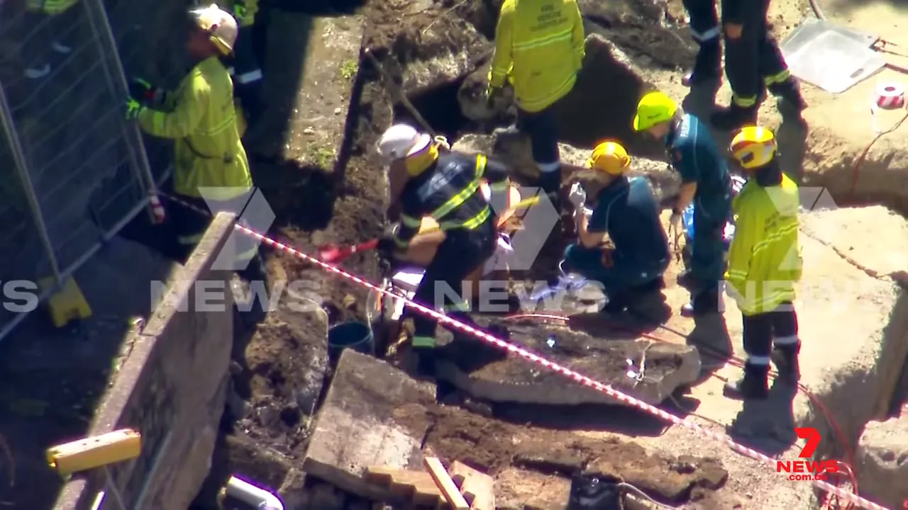 Clear aerial image of firefighters and paramedics treating a trapped construction worker amid fallen concrete slabs during a retaining wall collapse.