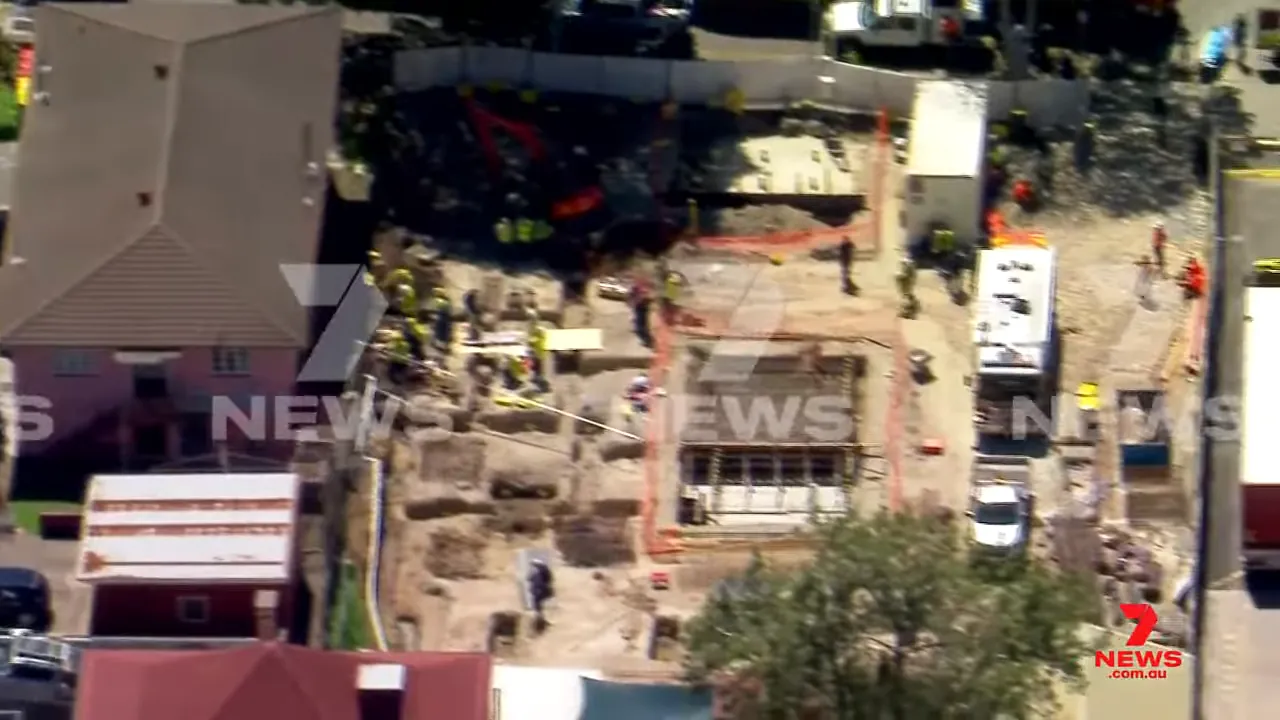 Aerial overview of a construction site with a collapsed retaining wall, trenches and emergency crews conducting a rescue