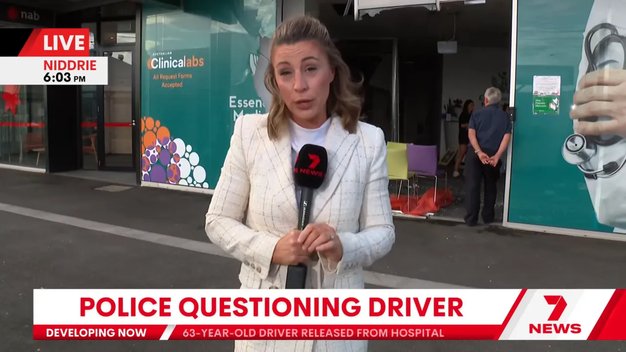 Reporter from Seven News standing outside the Niddrie medical centre with the damaged doorway, chairs and orange safety tarp visible inside