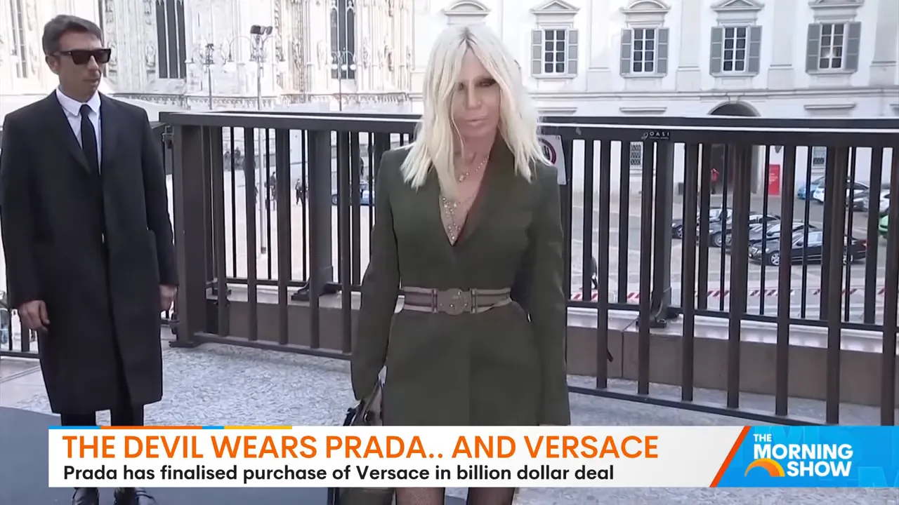 Blonde woman in a tailored green coat standing by a railing outside a venue, photographed front-on