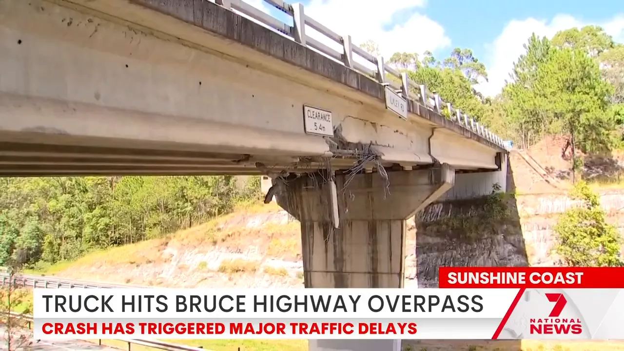 Damaged Bruce Highway overpass showing missing concrete and exposed reinforcement at a support column