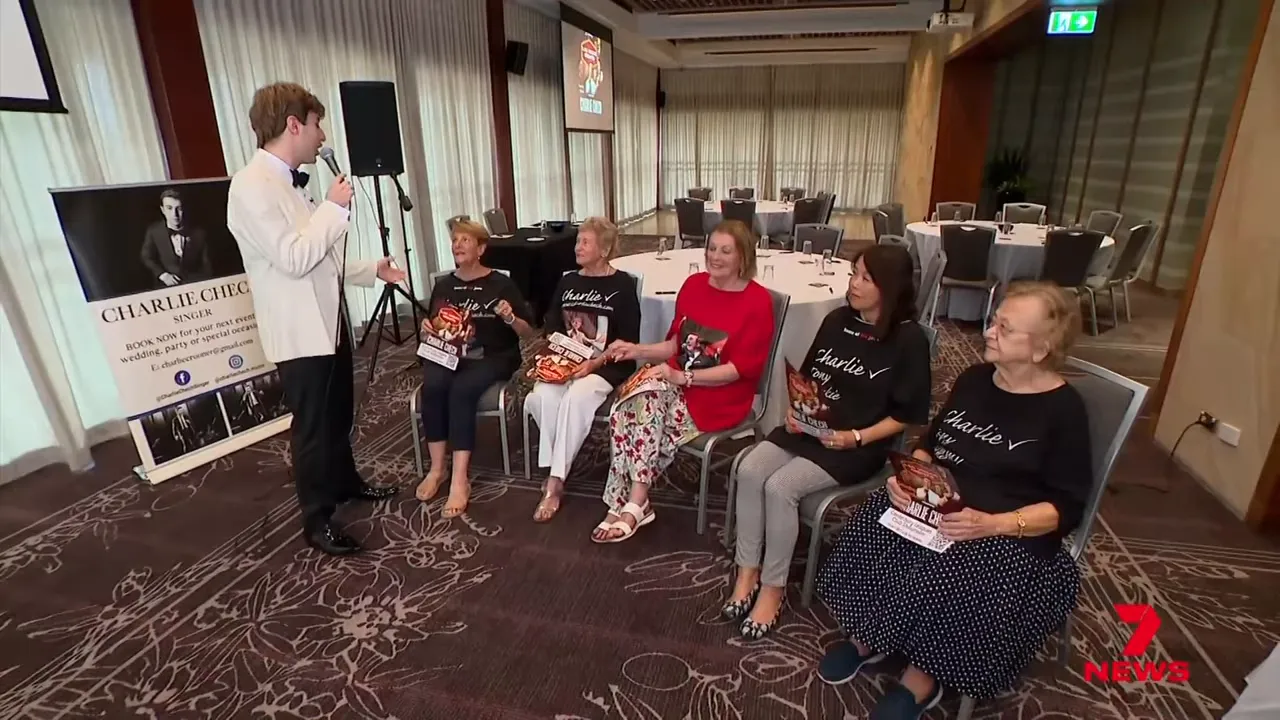 Wide shot of performer addressing a row of seated fans wearing matching shirts in a hotel function room