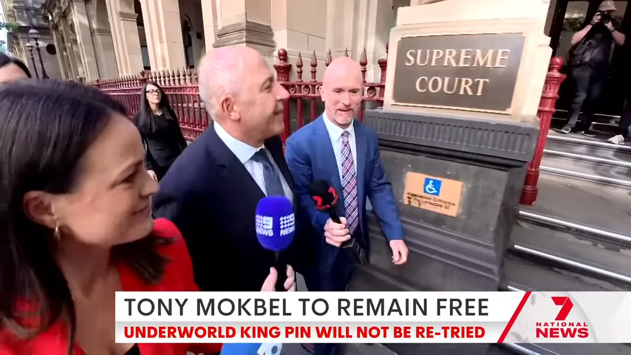 Man in a suit walking past a 'Supreme Court' sign with reporters and microphones gathered around outside the courthouse.