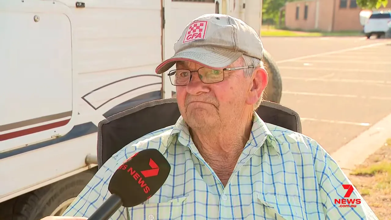 Seated elderly farmer in a cap being interviewed outdoors with a 7 News microphone close to frame