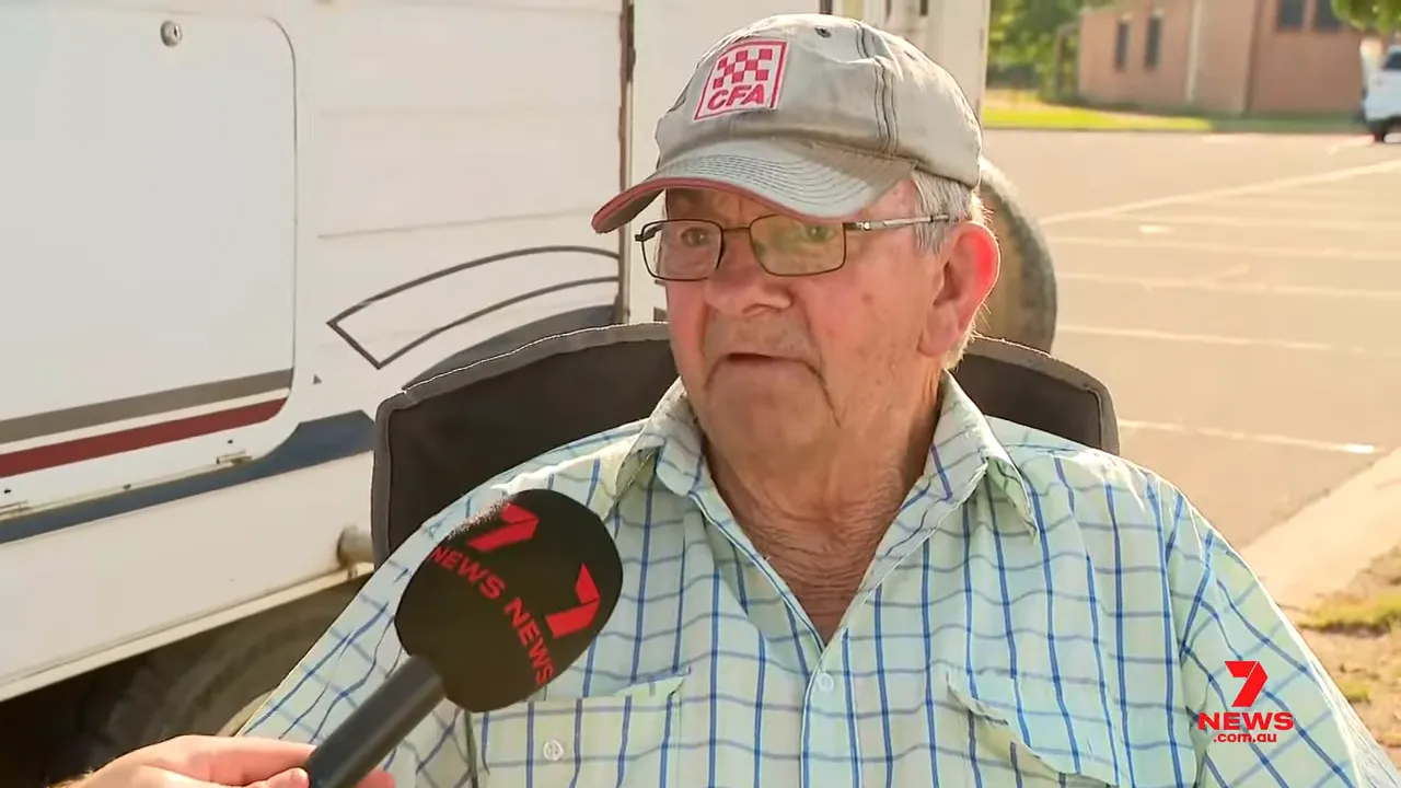Seated farmer being interviewed at a relief centre about pets and livestock with a 7 News microphone in frame