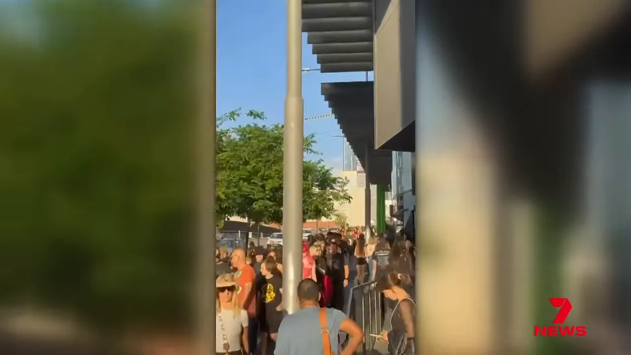 Long queue of fans along a barricaded concourse outside Marvel Stadium under stadium awnings