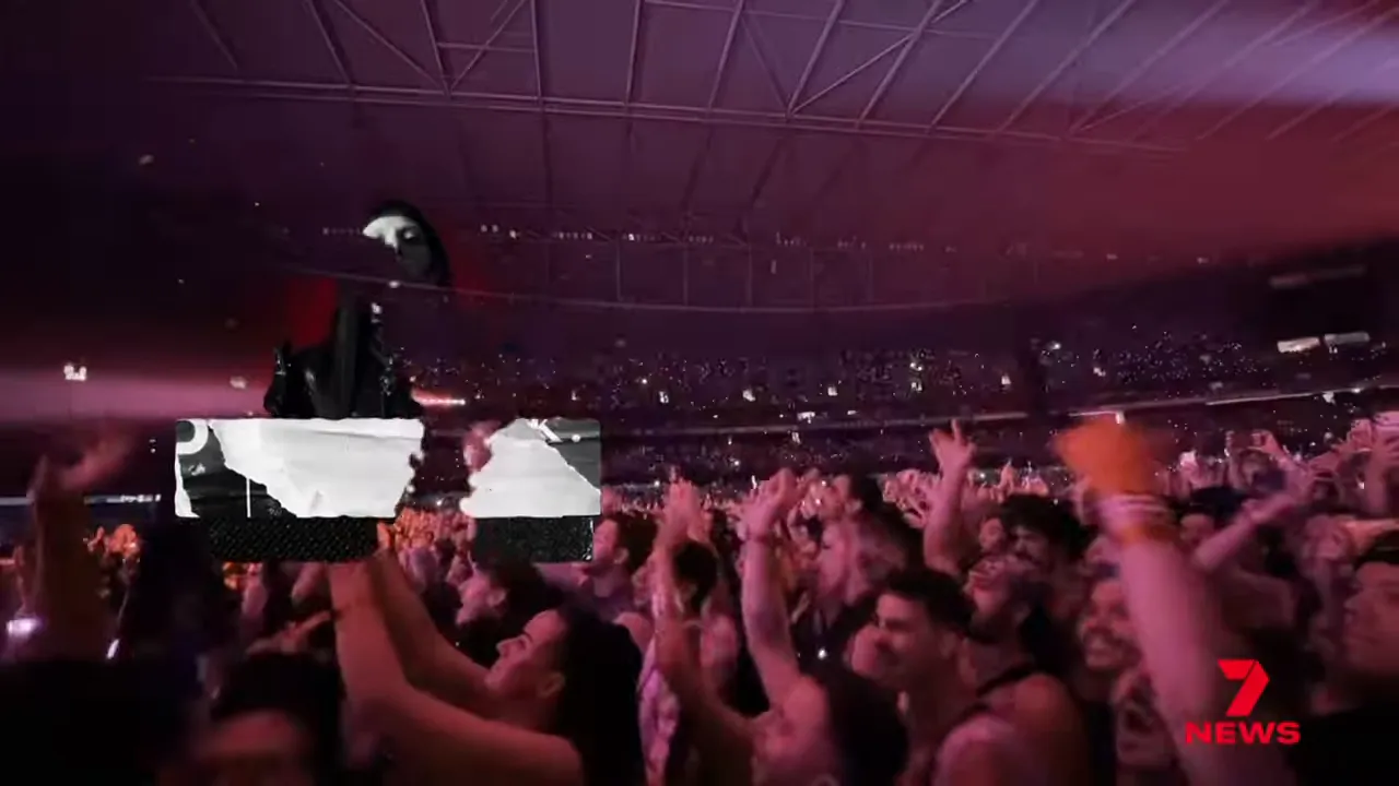 Packed concert crowd with hands raised toward the stage and the stadium roof visible overhead.
