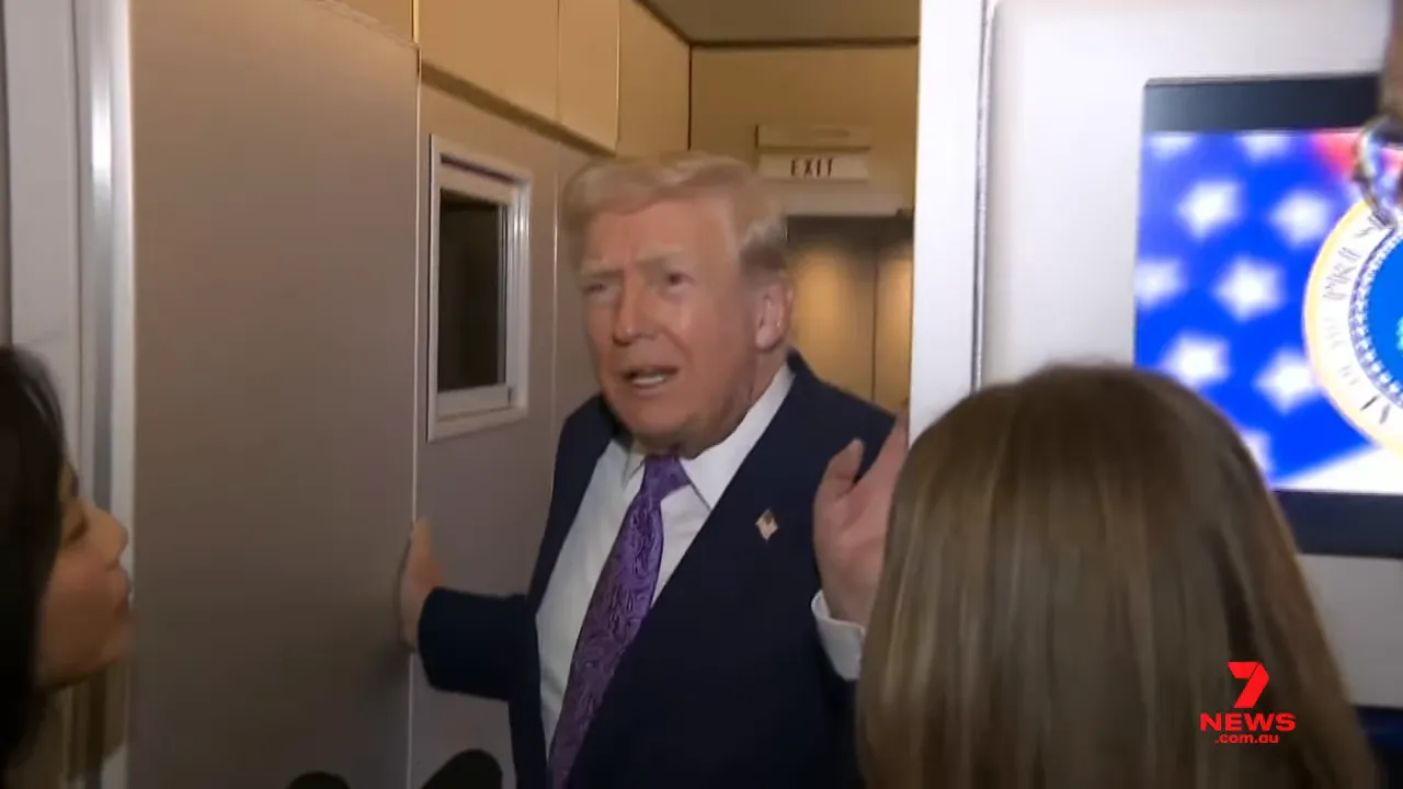 The president at a doorway speaking to reporters with microphones visible and a seal on a screen in the background