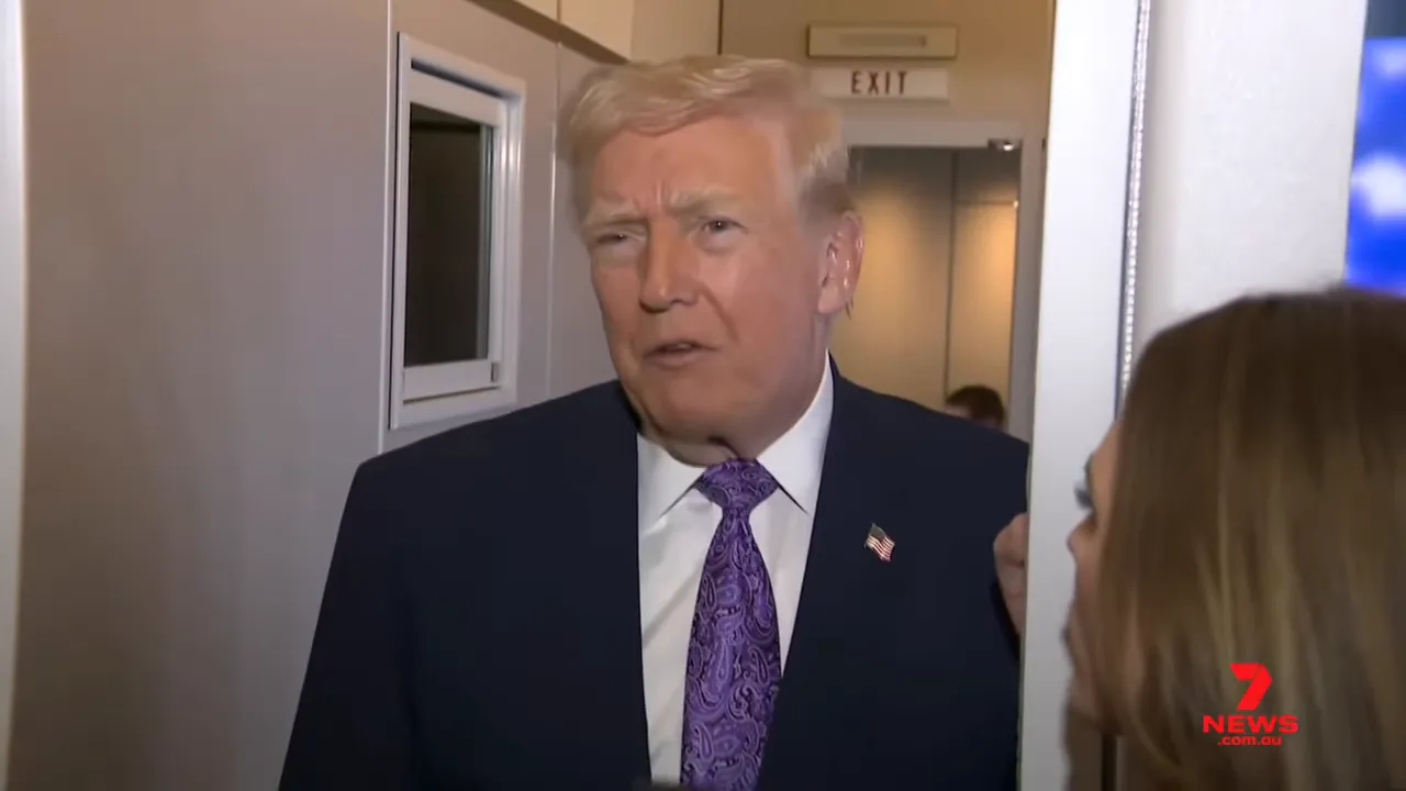 Crisp close-up of a man in a navy suit and purple tie speaking to reporters in a narrow doorway, microphones at hand